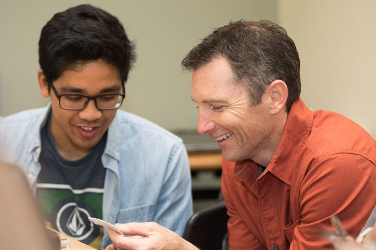 Two individuals seated closely, examining a small paper or card during discussion.