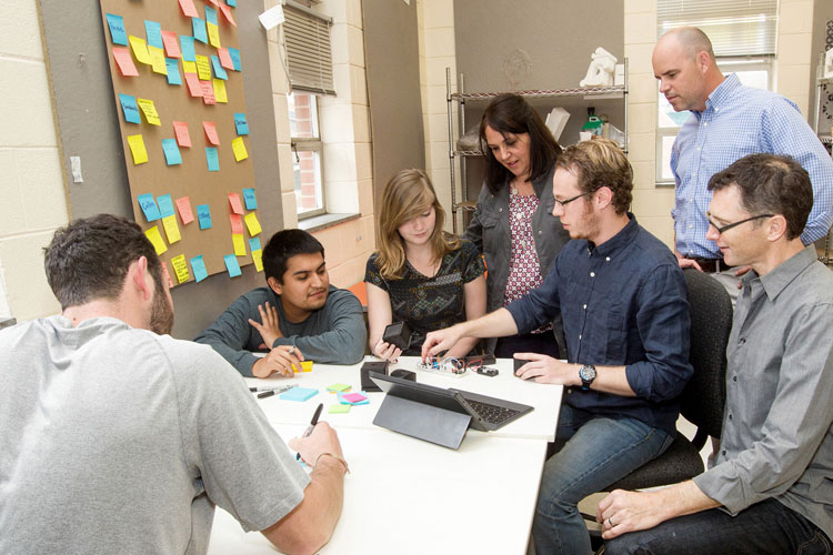 Group gathered around a table with notebooks and tablets, brainstorming with sticky notes.