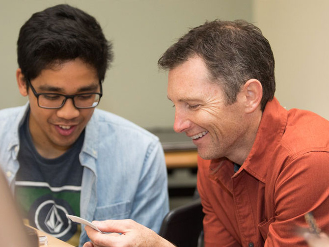 Two individuals seated closely, examining a small paper or card during discussion.