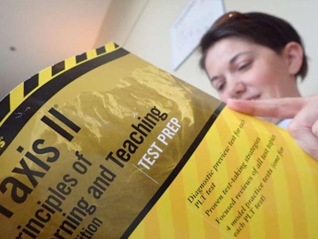 Close-up of a person reading a large gold and black test prep textbook, titled 'Praxis II Principles of Learning and Teaching.